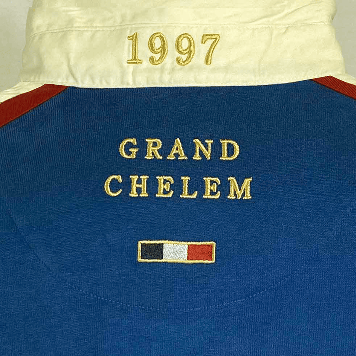 Close-up of the Ellis Rugby France Rugby 21 Club Collection 1997 Rugger, featuring a blue polo design with "1997" embroidered in gold on a white collar and "GRAND CHELEM" with a small French flag stitched below it, capturing the essence of a vintage rugby shirt celebrating the 1997 Grand Chelem.
