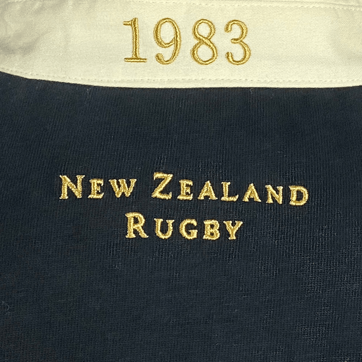 Close-up of the Ellis Rugby All Blacks 1983 Classic Rugby Shirt, featuring "1983" on the collar with "New Zealand Rugby" beautifully embroidered in gold on black fabric, reminiscent of an All Blacks shirt.