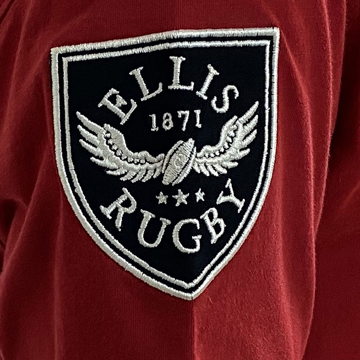 A close-up of the red fabric displays an embroidered patch reading "Ellis Rugby 1871," featuring a winged rugby ball and stars, echoing the classic style of an Ellis Rugby Canada Rugby 1932 T-Shirt.