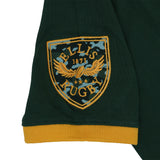 Embroidered Ellis Rugby crest with a camouflage pattern on a dark green Bomb Squad Rugby Polo sleeve with a mustard yellow cuff.