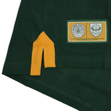 Close-up of a green Bomb Squad Rugby Polo by Ellis Rugby featuring a yellow side vent and a commemorative Bomb Squad rugby patch.