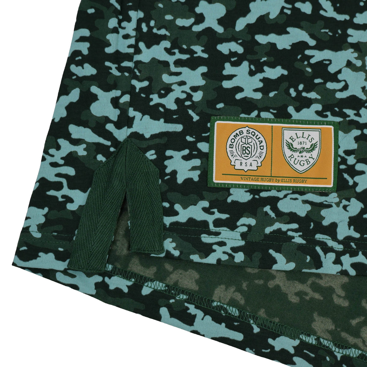 Hem of the Bomb Squad Bench T-Shirt by Ellis Rugby featuring a rectangular patch with the Bomb Squad and Ellis Rugby logos on a green camo-patterned fabric.