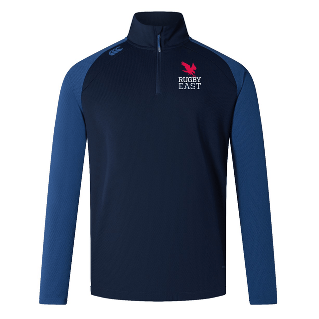 A navy and blue long-sleeve quarter-zip sweater featuring the "Rugby East" logo and a pink feather emblem on the upper left chest, along with a small white EMB Canterbury logo on the right shoulder. Ideal for training attire, this Rugby East Conference Elite First Layer by Canterbury incorporates VapoDri technology to keep you comfortable.