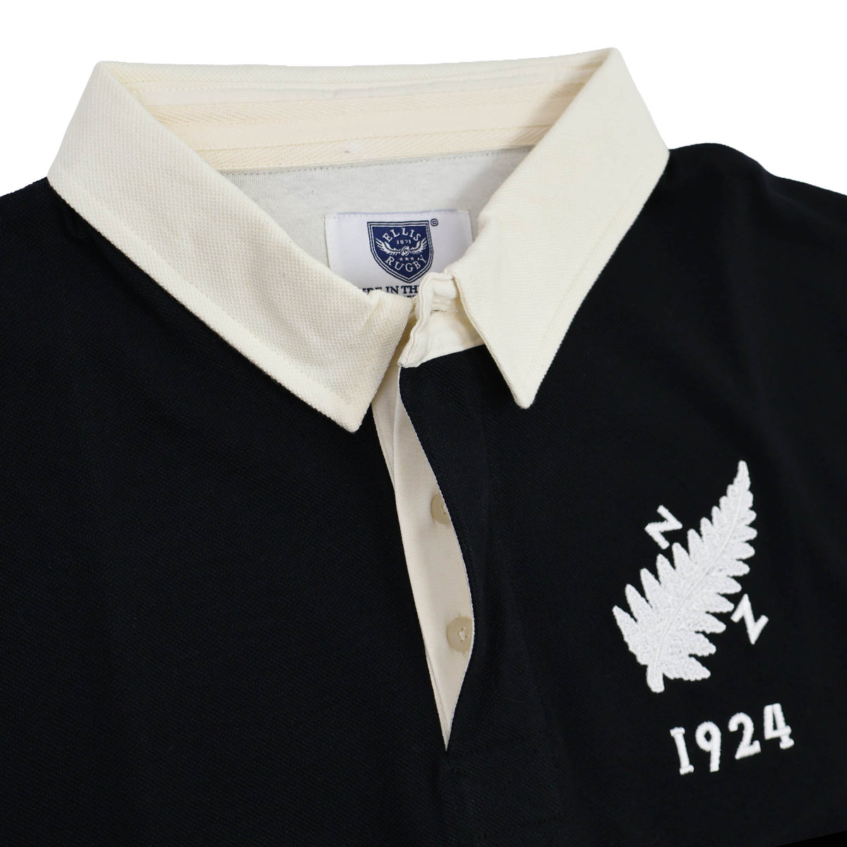 Close-up of the New Zealand Rugby 1924 Polo by Ellis Rugby—a black rugby shirt with a white collar, detailed with an embroidered white fern leaf, “NZ,” and “1924” on the chest. This classic polo pays tribute to New Zealand’s authentic rugby heritage.