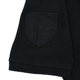 A close-up of the black sleeve of the New Zealand Rugby 1924 Polo by Ellis Rugby reveals an embroidered patch featuring “Ellis Rugby 1871” alongside an eagle clutching a rugby ball, reflecting the enduring rugby heritage embodied by Ellis Rugby.