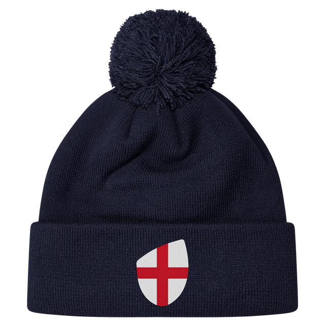 The England Shield Pom Pom Beanie by EMB Canterbury is a navy blue beanie featuring a prominent shield emblem with a red cross on a white background.
