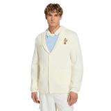 A young man models the France FFR 120 Year Cardigan by adidas, featuring a chest patch, over a pale blue shirt and white pants, against a plain white background—showcasing classic French rugby heritage.