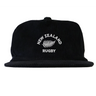The EMB Weld Nations of Rugby New Zealand Corduroy Field Trip Cap is a vintage-style black hat featuring "NEW ZEALAND RUGBY" and a white fern embroidered on the front.