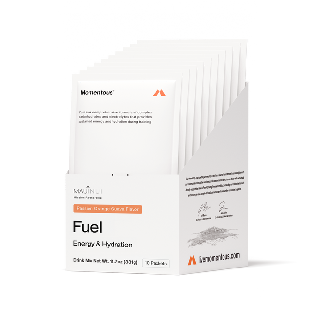 A white box labeled "Momentous Fuel 10-Travel Packs" holds 10 packets of Passion Orange Guava carb electrolyte formula for sustained energy and hydration during endurance exercise. The box features the Momentous brand and livemomentous.com.