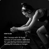 A woman in athletic wear rides a stationary bike indoors, wearing headphones. In the lower left, instructions explain how to mix Momentous Fuel by Momentous for sustained energy during intense exercise.