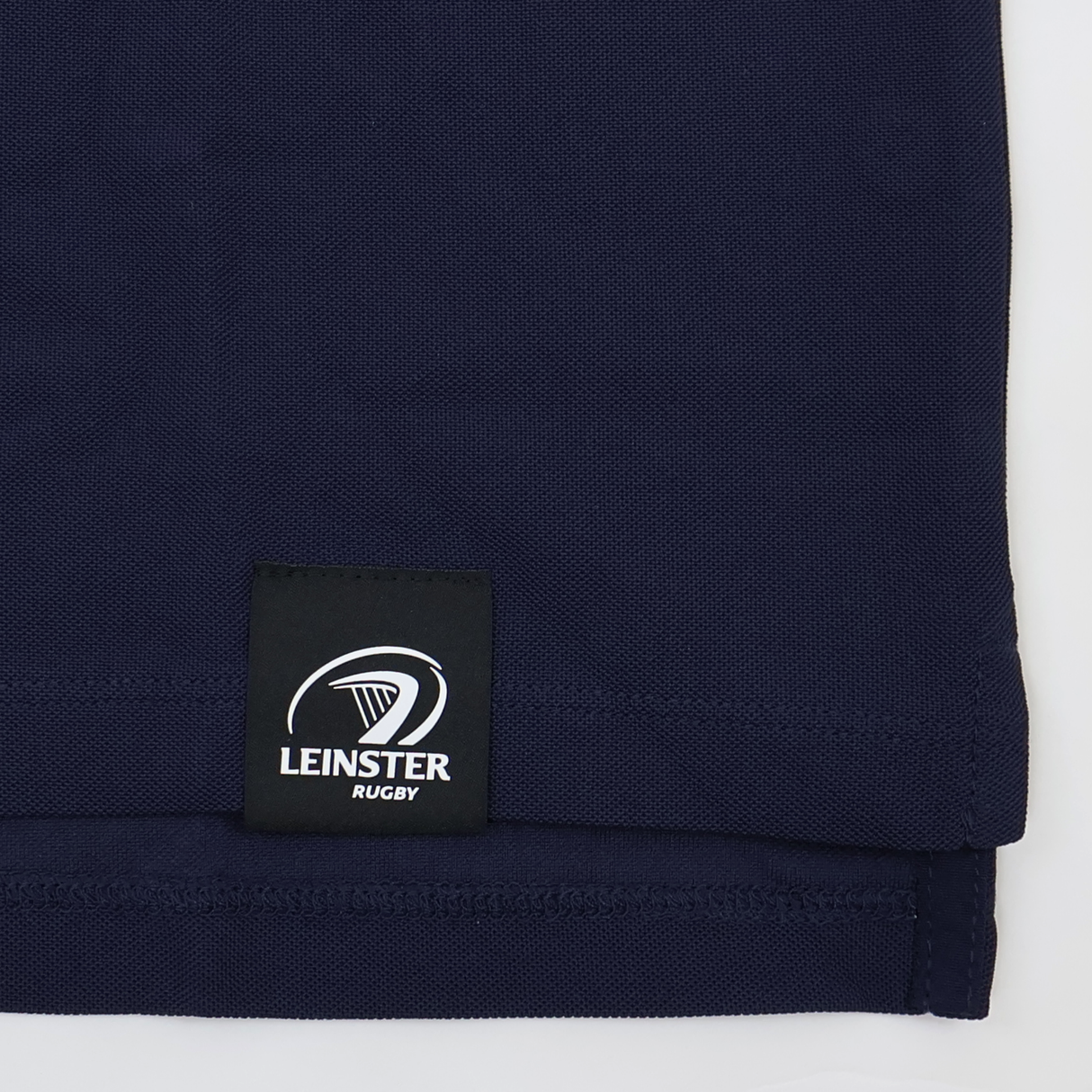 A close-up of the hem of the Leinster 24/25 Club Essential Polo by Castore, featuring a sewn-on label with the Leinster Rugby logo and text.