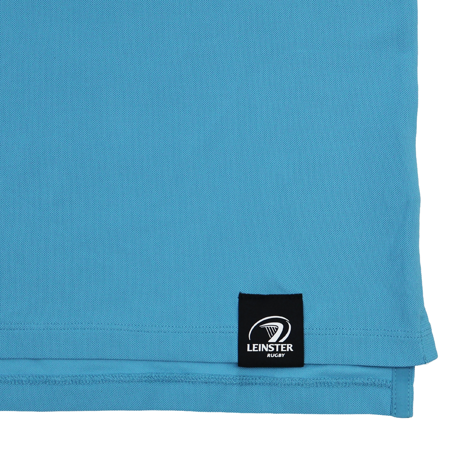 Close-up of the lower hem of the Castore Leinster 24/25 Club Essential Polo in light blue, showing a black label with the Leinster Rugby logo in white.