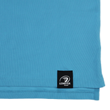 Close-up of the lower hem of the Castore Leinster 24/25 Club Essential Polo in light blue, showing a black label with the Leinster Rugby logo in white.