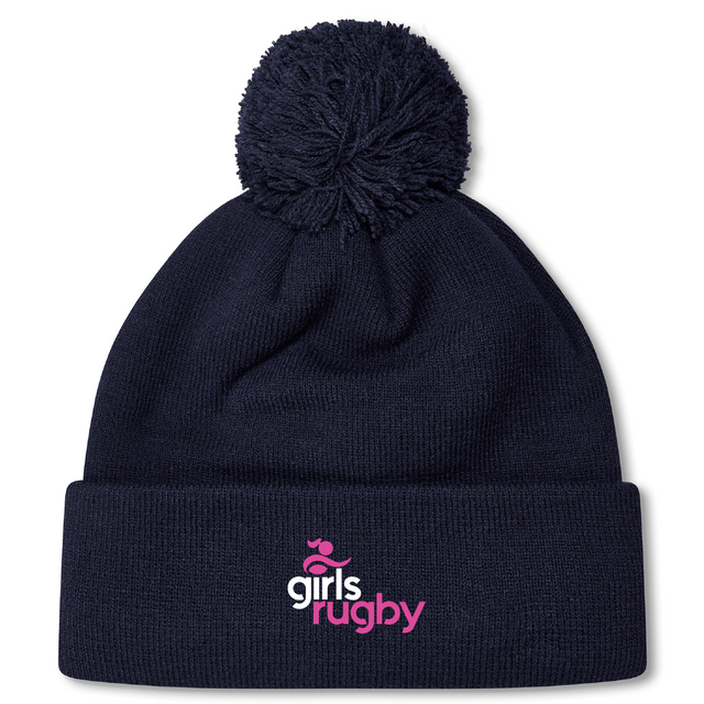 The Girls Rugby Pom Pom Beanie by Canterbury, featuring a navy blue knit design with a pom-pom and the "girls rugby" logo in pink and white on the cuff, is perfect for chilly days. Brand: EMB Canterbury.