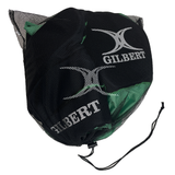A black mesh Gilbert drawstring bag holds sports balls and a padded Gilbert Contact Top Pro rugby shirt, all featuring the Gilbert logo.