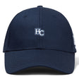 The Holy Cross Flexfit Drill Cap by EMB Canterbury is a navy blue cap with a white and blue "HC" embroidered logo on the front.