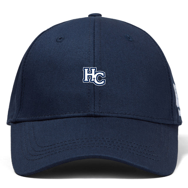 The Holy Cross Flexfit Drill Cap by EMB Canterbury is a navy blue cap with a white and blue "HC" embroidered logo on the front.