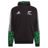Introducing the Maori All Blacks Performance Hoodie by adidas, a striking black rugby hoodie flaunting "Māori All Blacks" text and a silver fern emblem. This performance piece proudly displays the iconic Adidas logo, complemented by white stripes and vibrant green Māori patterns on its sleeves and hood, perfectly merging style with athletic heritage.