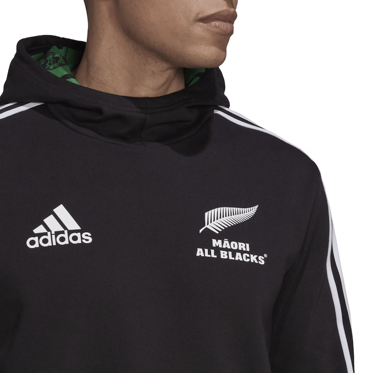 Dressed in the Maori All Blacks Performance Hoodie by adidas, featuring a sleek black design with iconic white stripes and showcasing the "Māori All Blacks" logo prominently on the chest, this individual embodies both style and team spirit.