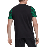 A man is wearing the Maori All Blacks Performance Polo by adidas, featuring a black T-shirt with green patterned sleeves. He pairs it with black pants adorned with white stripes. The ensemble merges style and comfort while staying cool thanks to the moisture-wicking AEROREADY technology, echoing the vibrant energy of the Maori All Blacks.