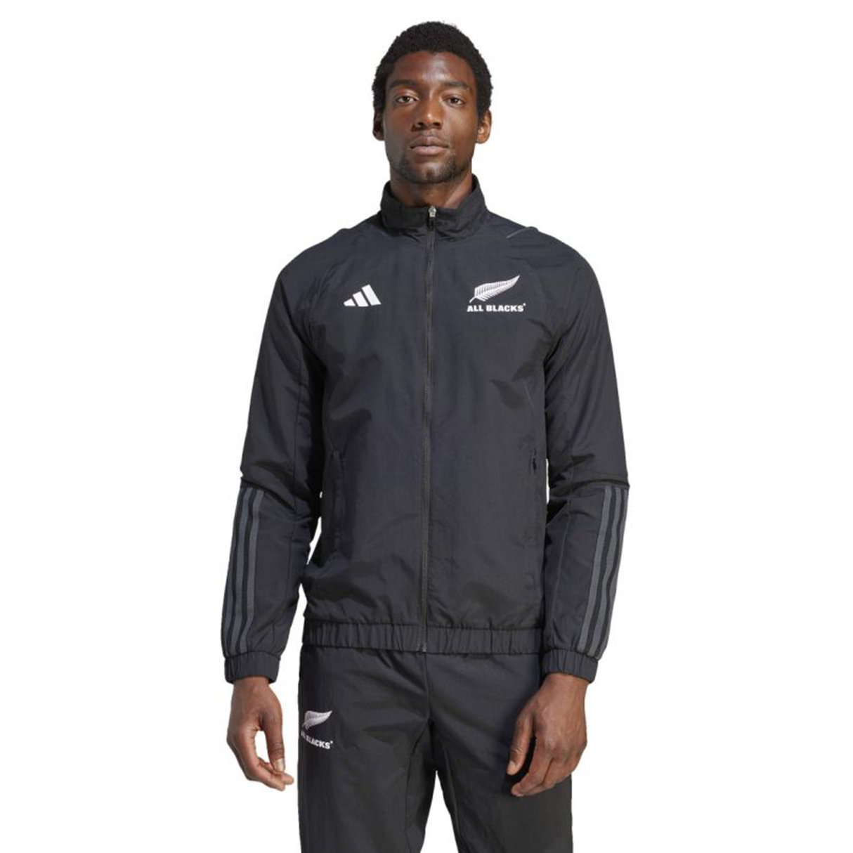 Dressed in the All Blacks Presentation Jacket by adidas, a person showcases rugby fashion effortlessly with its sleek black design and white logos.