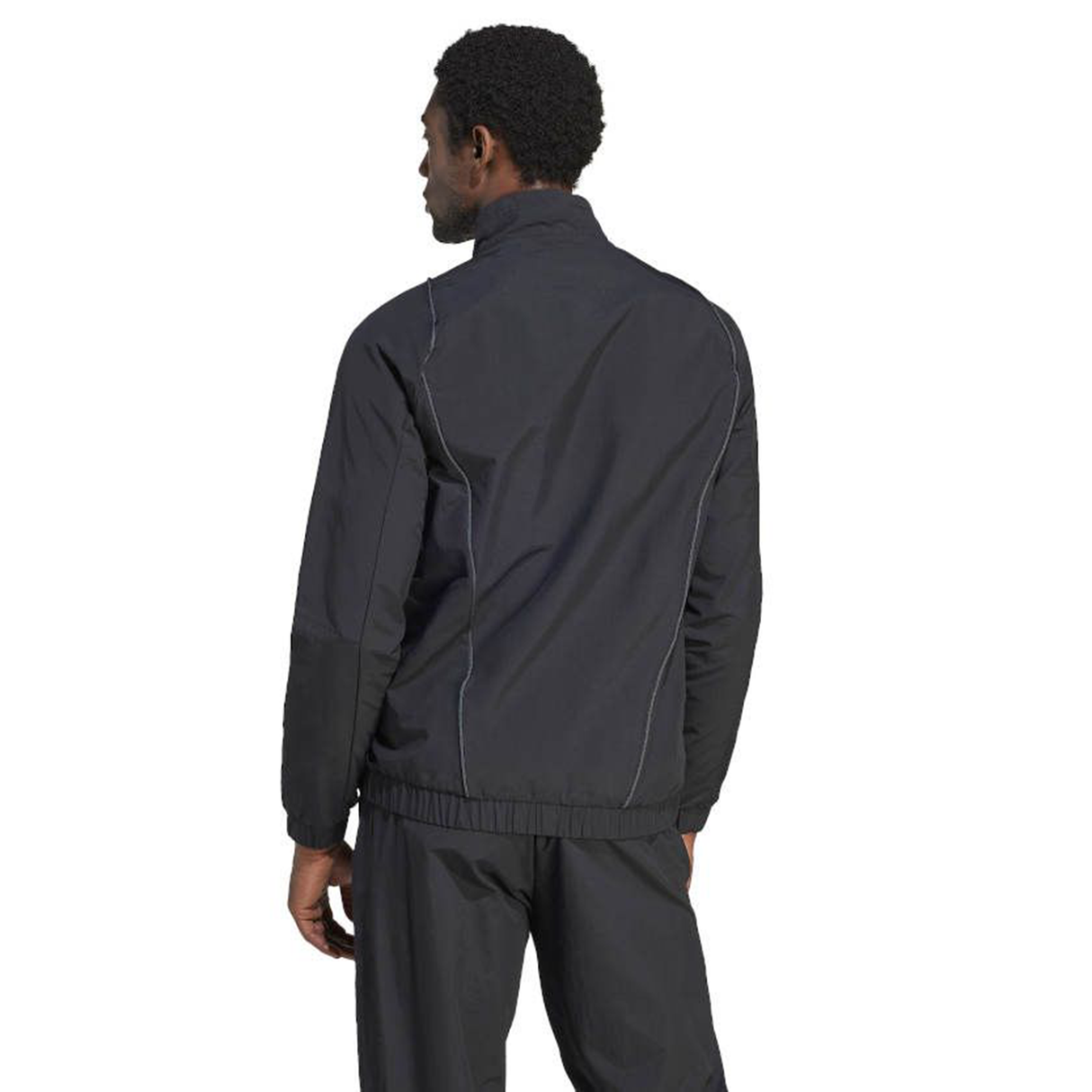 A man stands with his back turned, wearing an All Blacks Presentation Jacket by adidas, featuring a dark tracksuit style inspired by rugby fashion.
