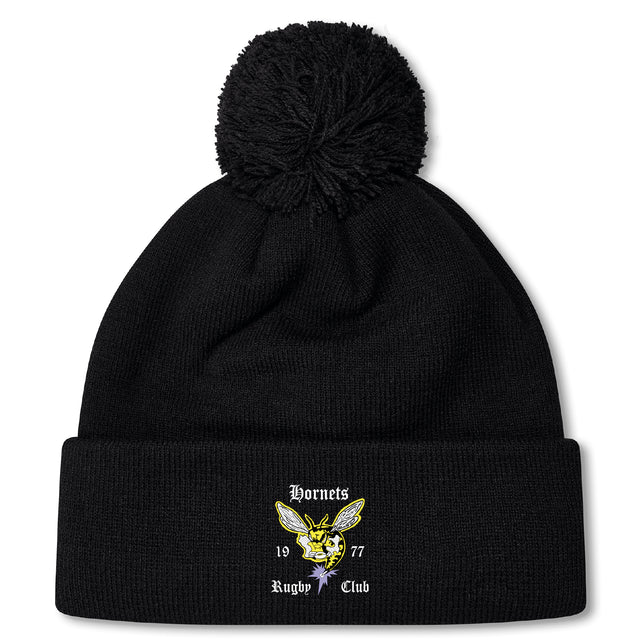 The Hornets Rugby Club Pom Pom Beanie by EMB Canterbury is a black fleece-lined knit hat with a pom-pom and embroidered "Hornets Rugby Club 1977" logo—perfect for rugby fans.