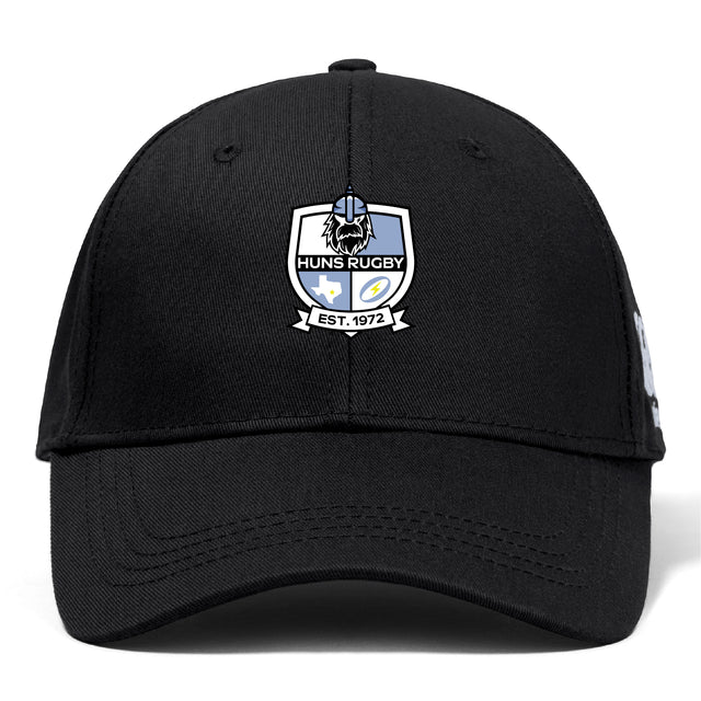 The Austin Huns Rugby Flexfit Drill Cap by EMB Canterbury is a black curved brim cap featuring the Huns Rugby embroidered logo patch and "EST. 1972" on the front.