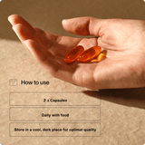A hand holds two orange capsules; instructions say to take 2 Momentous Omega-3 capsules daily with food and store in a cool, dark place for best quality. Supports brain and heart health. Brand: Momentous.