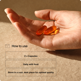 A hand holds two orange capsules; text reads: Take two Momentous Omega-3 Travel Packs daily with food and store in a cool, dark place. Supports cardiovascular health.