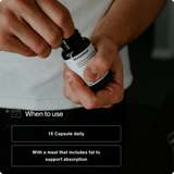 A person opens a bottle of Momentous Vitamin D3 5000 IU by Momentous, labeled with instructions to take one capsule daily with a fat-containing meal for better absorption to support immune function and bone strength.