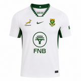 The Springboks 26/27 Replica Away Jersey by Nike is a white South Africa rugby jersey with green accents, featuring the Springbok logo, Rugby badge, FNB sponsor, Nike logo, and a small South African flag on the sleeve.