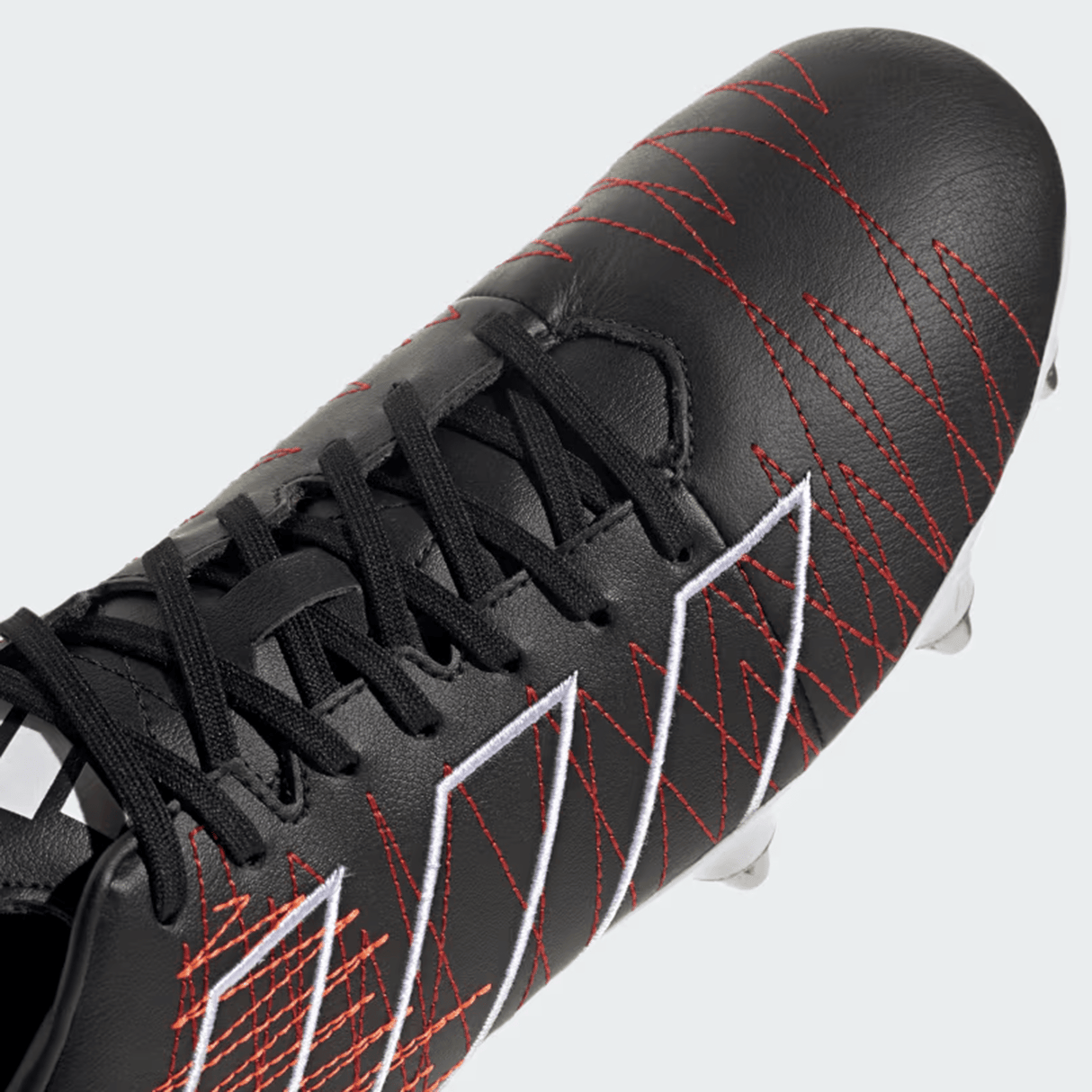 Close-up of an adidas Kakari Elite SG 24 Rugby Cleat in Core Black/Core Black/Better Scarlet, featuring red stitching, white geometric patterns, black laces, and metal studs.