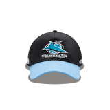 Classic Sportswear's Sharks NRL 25/26 Media Cap in black with a blue brim features an embroidered "Sharks" and stylized shark logo on the front, showcasing sporty sophistication.
