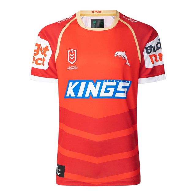 The Dolphins NRL 25/26 Replica Home Jersey by Classic Sportswear showcases a red and orange design with the iconic "KINGS" logo, a striking dolphin graphic, and white sponsor names on the sleeves, proudly embodying the Dolphins NRL spirit.