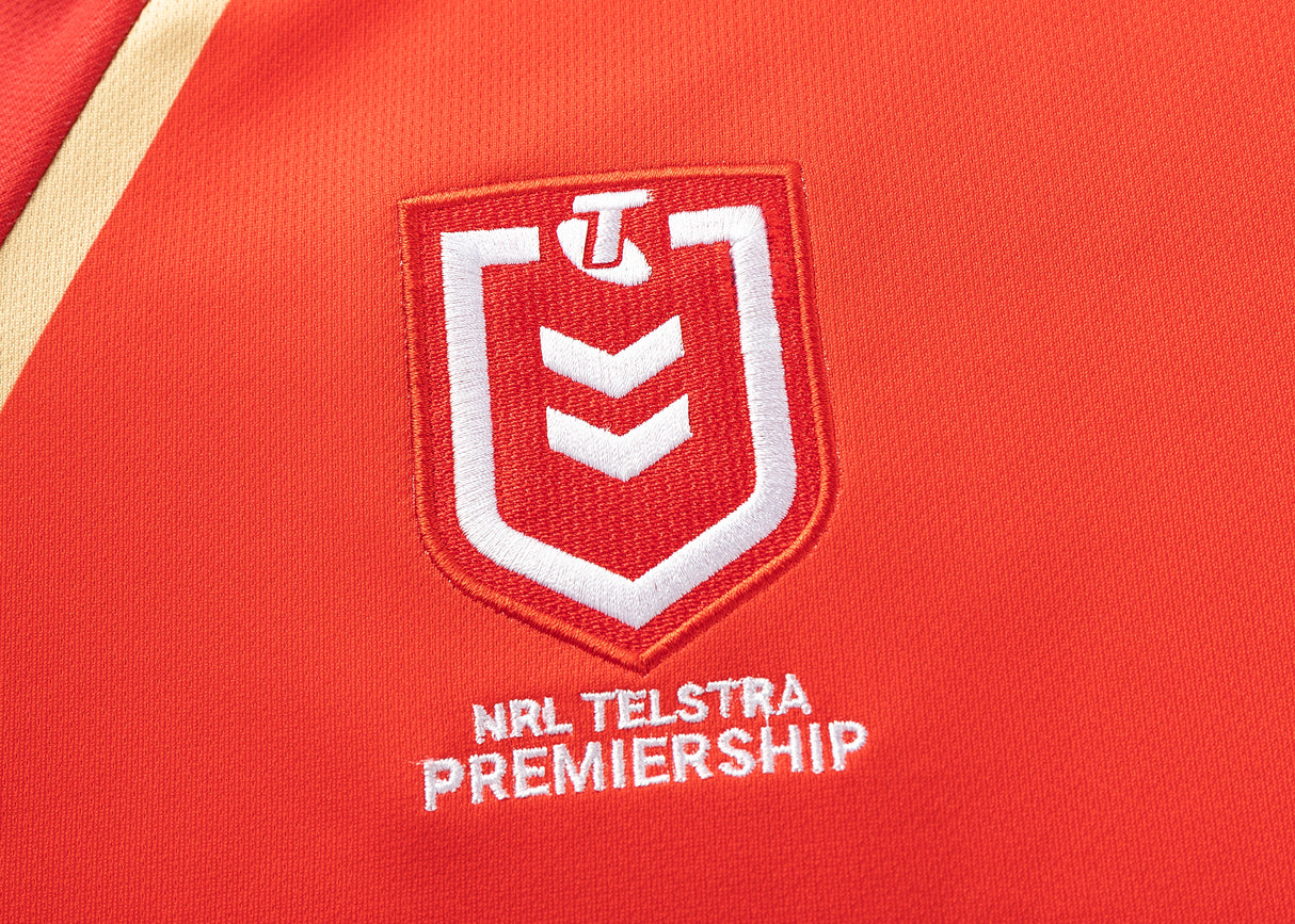 Close-up of the NRL Telstra Premiership logo on a red fabric, featuring a white shield with a stylized "T" and chevron, as seen on the Dolphins NRL 25/26 Replica Home Jersey by Classic Sportswear.