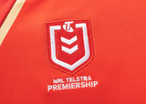 Close-up of the NRL Telstra Premiership logo on a red fabric, featuring a white shield with a stylized "T" and chevron, as seen on the Dolphins NRL 25/26 Replica Home Jersey by Classic Sportswear.