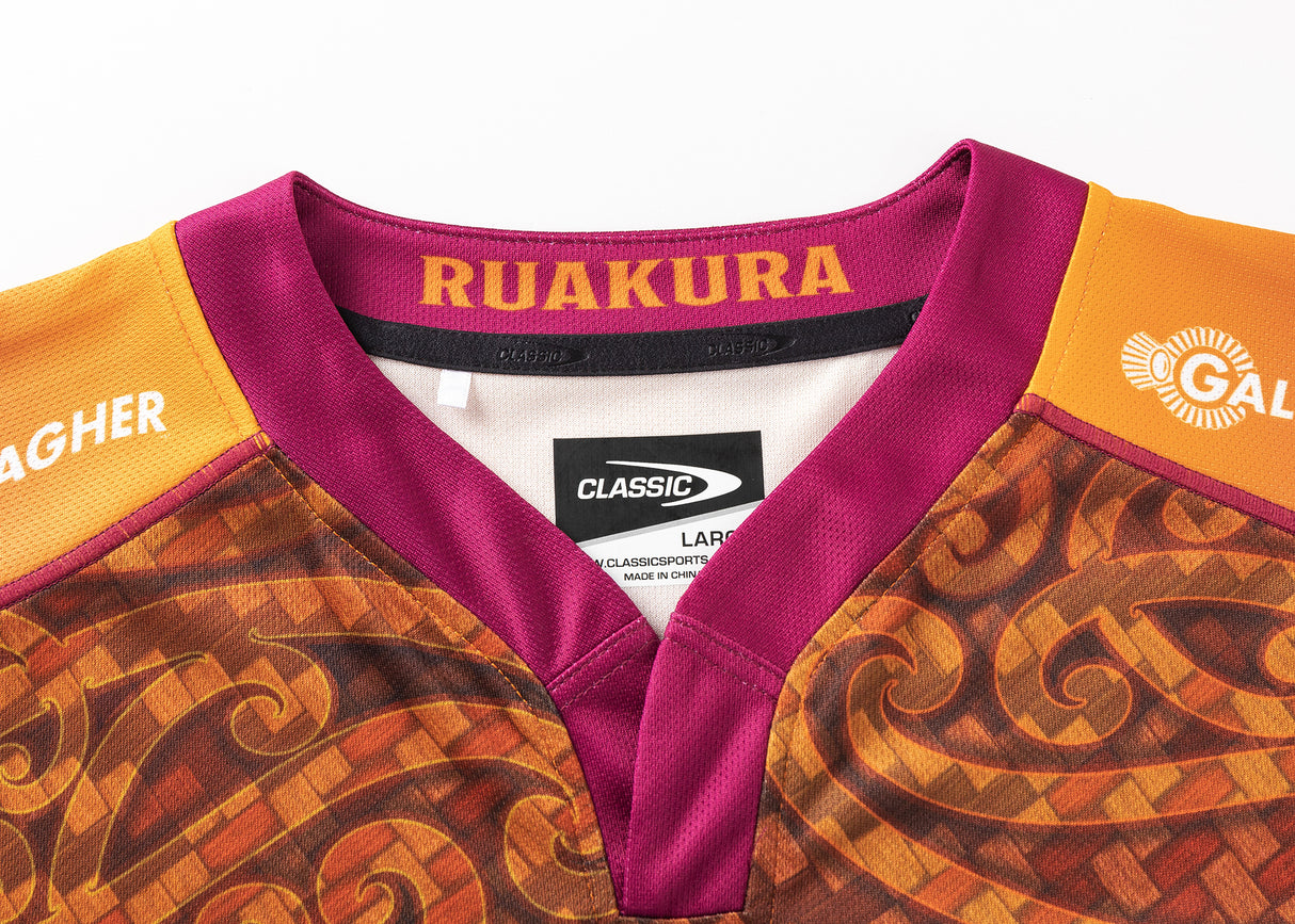 A close-up of the maroon and orange Gallagher Chiefs Super Rugby Replica Training Jersey 25/26 by Classic Sportswear, adorned with decorative patterns. The inside collar reads "RUAKURA," and labels are attached, making it perfect for fans to display their support.