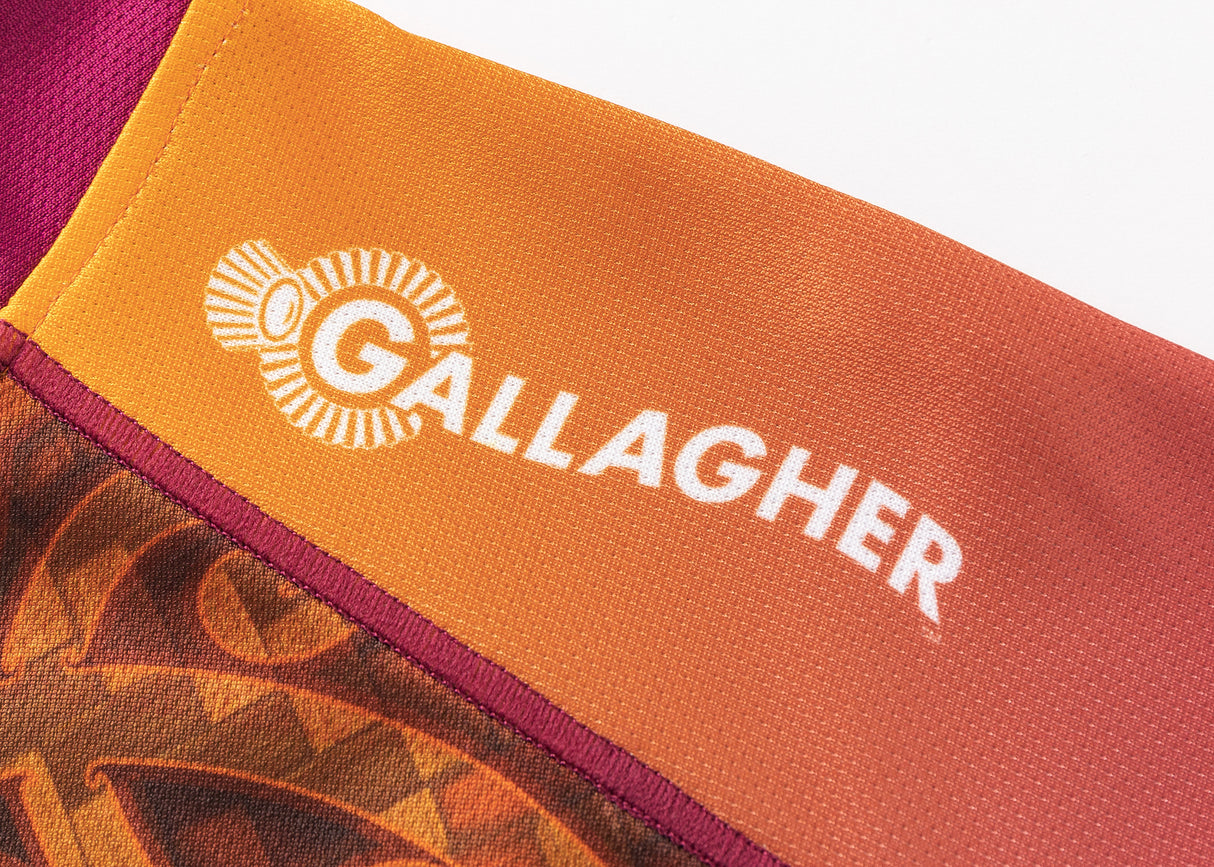 A close-up of an orange and red fabric, likely the Gallagher Chiefs Super Rugby Replica Training Jersey 25/26 by Classic Sportswear, with "GALLAGHER" and a logo printed in white.
