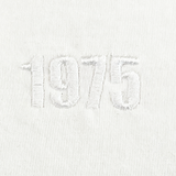 The EMB Alpha Broder USA Rugby Elevated Throwback Tonal Comfort Tee showcases a throwback logo with "1975" intricately embroidered in raised white thread at the center on white fabric, crafted from premium ring-spun USA cotton.
