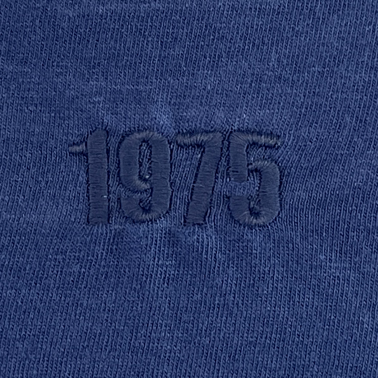 Close-up of the USA Rugby Elevated Throwback Tonal Comfort Tee by EMB Alpha Broder, featuring "1975" in bold dark blue embroidery. Crafted from soft ring-spun USA cotton.