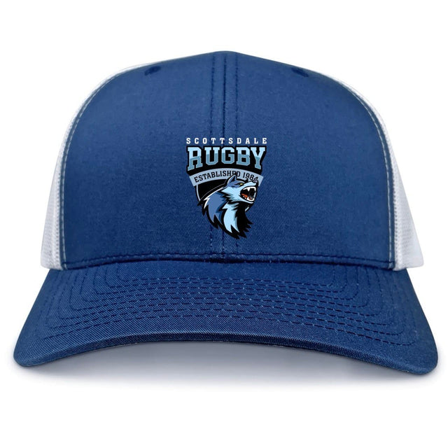 The Scottsdale Rugby Royal Retro Trucker Cap by EMB S&S Activewear features blue and white panels, an embroidered "Scottsdale Rugby" logo with a wolf and "Established 1986" on the front, plus a classic snapback closure.