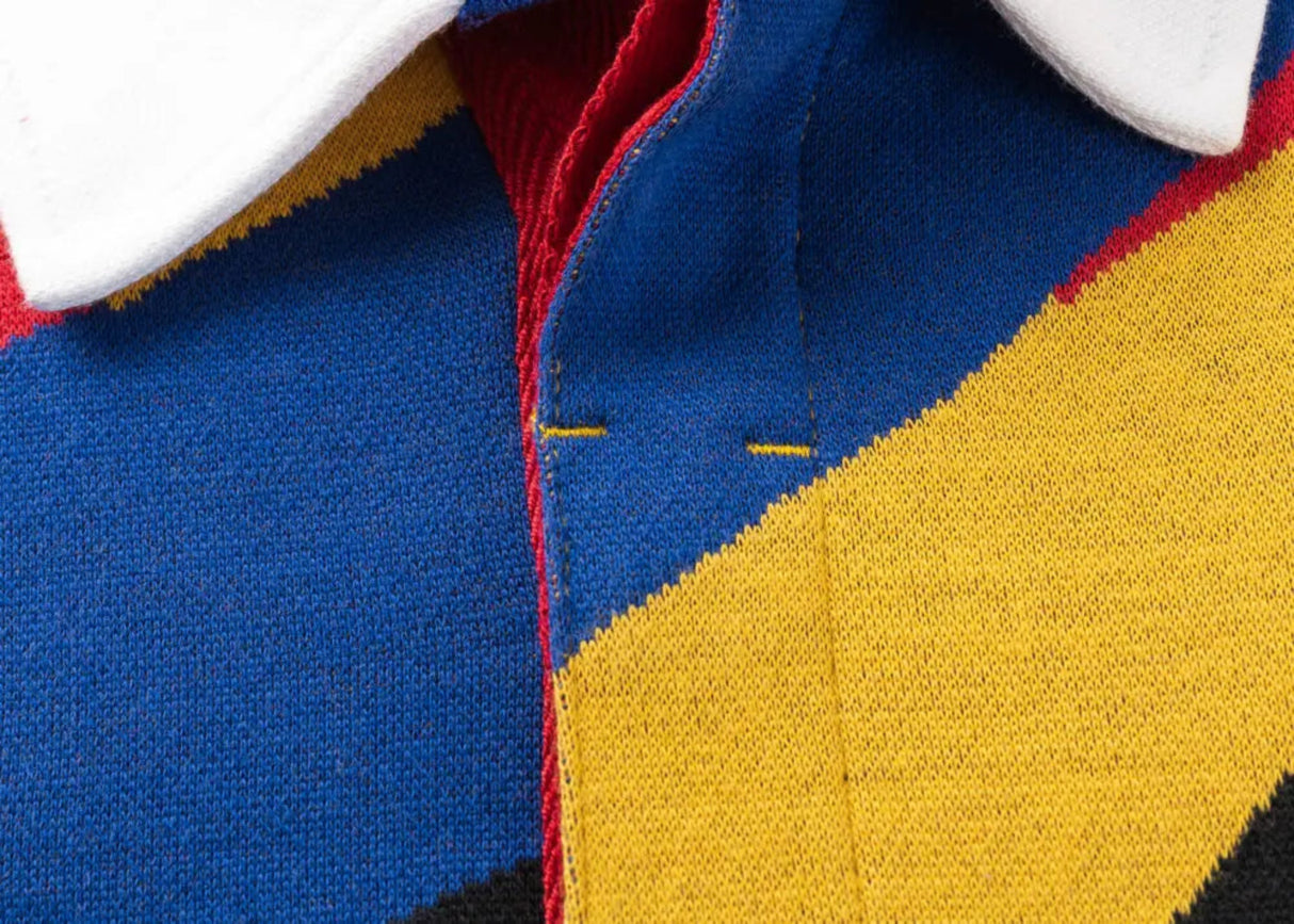 Close-up of a colorful knit fabric with geometric patterns in blue, yellow, red, and black, reminiscent of the Limited Edition Gallagher Chiefs Super Rugby 25/26 Retro Jersey by Classic Sportswear. A white collar peeks from the top.