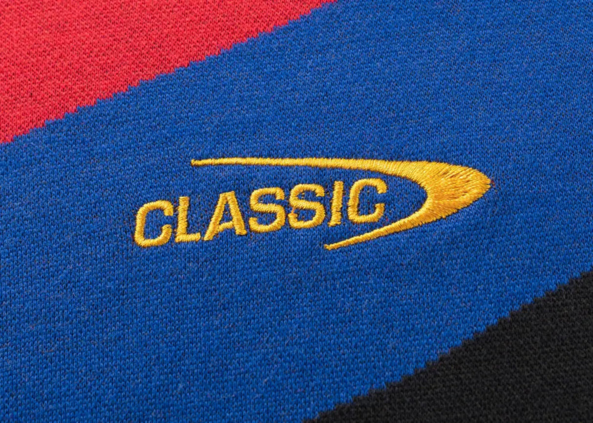 A close-up of a fabric with blue, red, and black stripes features the word "CLASSIC" embroidered in yellow with a swoosh design, similar to the Limited Edition Gallagher Chiefs Super Rugby 25/26 Retro Jersey by Classic Sportswear.