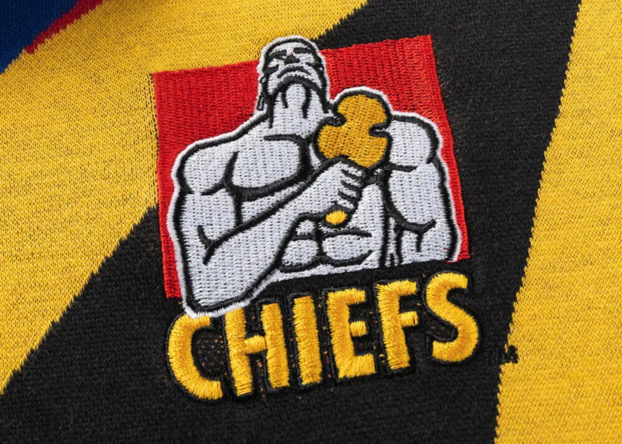 An embroidered patch featuring a muscular figure with a yellow object and "Gallagher Chiefs" on textured fabric adds nostalgic charm to Classic Sportswear's Limited Edition Gallagher Chiefs Super Rugby 25/26 Retro Jersey.