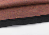 Close-up of a folded fabric with a retro jersey vibe, featuring a brown weave pattern and black edge trim resembling the spirited style of Classic Sportswear's Limited Edition Gallagher Chiefs Super Rugby 25/26 Retro Jersey, resting on a flat surface.