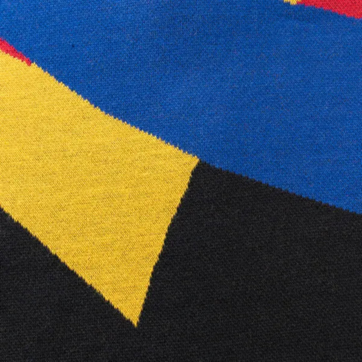 Close-up of a fabric featuring a geometric pattern in blue, yellow, black, and red sections, akin to the Limited Edition Gallagher Chiefs Super Rugby 25/26 Retro Jersey by Classic Sportswear.