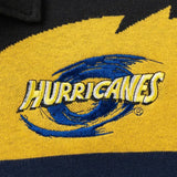 The Limited Edition Hurricanes Super Rugby 25/26 Retro Jersey by Classic Sportswear features a close-up of an embroidered "Hurricanes" logo in yellow and blue. The swirl design on the yellow and black fabric captures the energy of Hurricanes Super Rugby, enhancing its retro jersey charm.