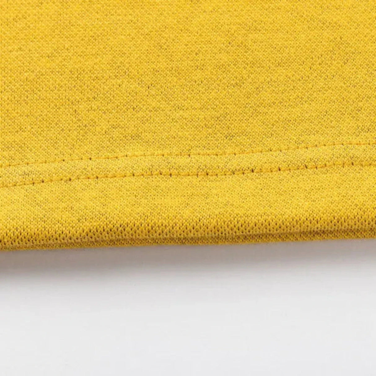 Close-up of a yellow fabric featuring edge stitching, reminiscent of Classic Sportswear's Limited Edition Hurricanes Super Rugby 25/26 Retro Jersey, against a white background.