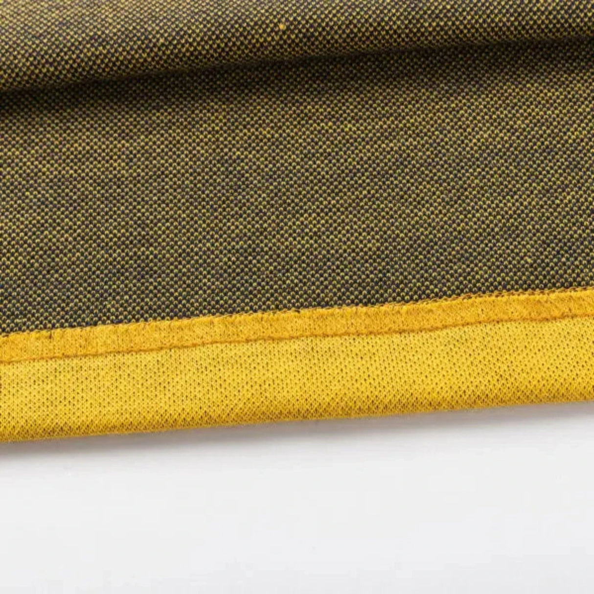 Close-up of a textured fabric with a yellow edge, resembling the Limited Edition Hurricanes Super Rugby 25/26 Retro Jersey by Classic Sportswear. The darker shade features small dotted patterns, capturing classic sportswear's essence.
